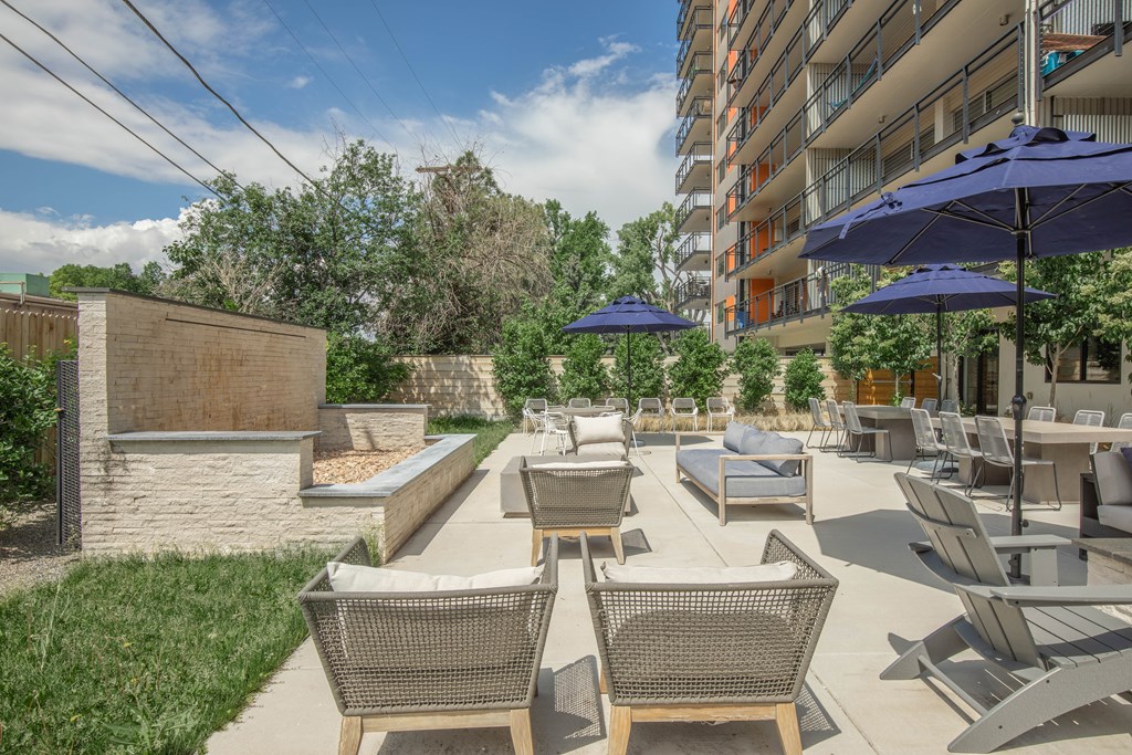 A patio with chairs and umbrellas is surrounded by a grassy area and a building.