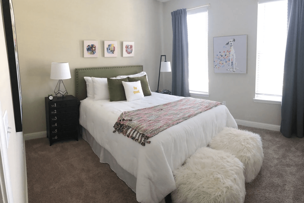 A bedroom with a large bed and a white fluffy ottoman.