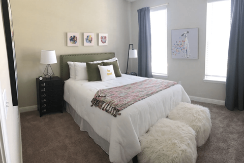 A bedroom with a large bed and a white fluffy ottoman.