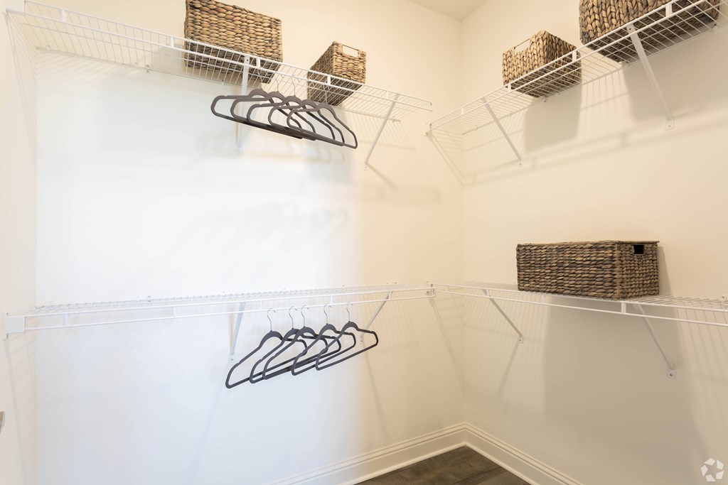 A white closet with clothes hangers and baskets.