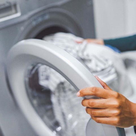 A person is loading a white shirt into a washing machine.