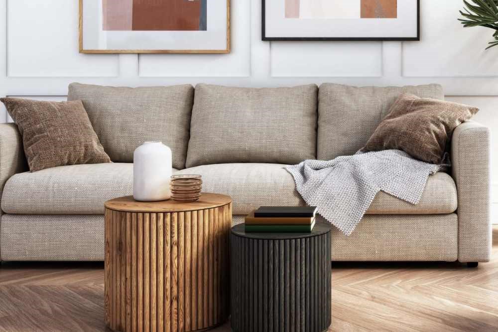 A beige couch with a grey throw and a white candle on a wooden table.