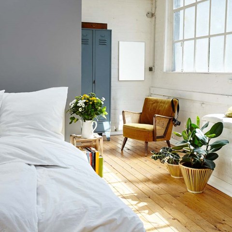 A bed with white sheets and pillows is in a room with a wooden floor and a chair.