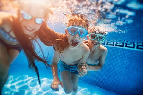 Two children wearing goggles and swimming in a pool.