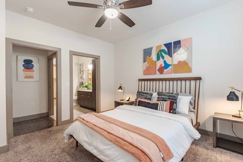 A bedroom with a bed, a ceiling fan, and a painting on the wall.