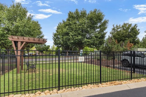 A black fence surrounds a green park area with a wooden pergola.