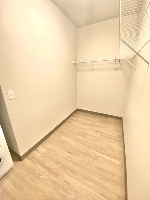 A white closet with a wooden floor and a white shelf.