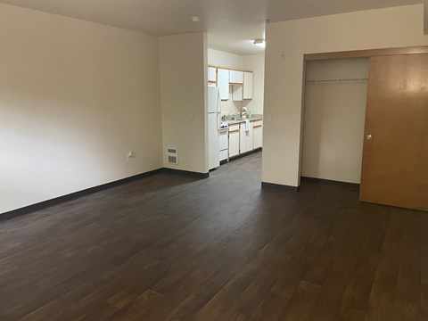 A room with wooden floors and a kitchen in the background.