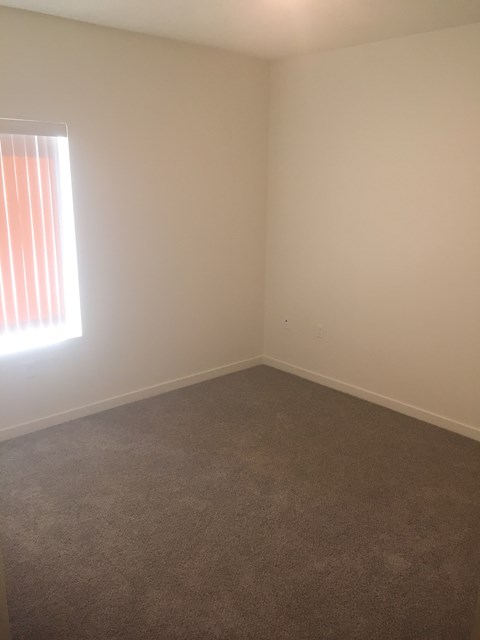 A room with a carpeted floor and a window with red curtains.