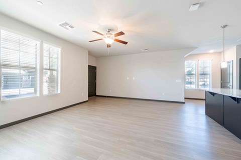 A spacious living room with a ceiling fan and large windows.