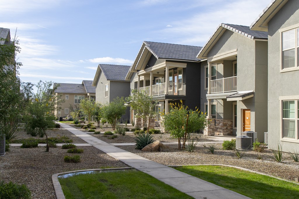 a row of apartment buildings with a sidewalk and grass