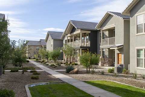 a row of apartment buildings with a sidewalk and grass