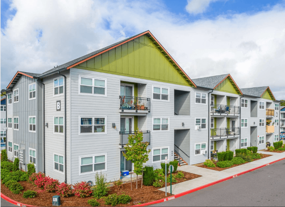 A row of modern apartments with balconies and flower beds in front.