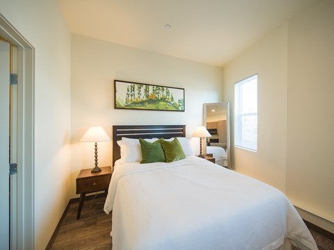 A bedroom with a large bed, a nightstand with a lamp, and a painting on the wall.