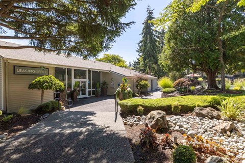 A leasing office is surrounded by a landscaped area with rocks and shrubs.