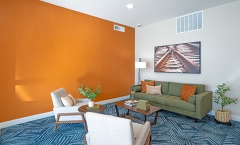 A living room with a green couch, a white chair, and a painting of a railway track on the wall.