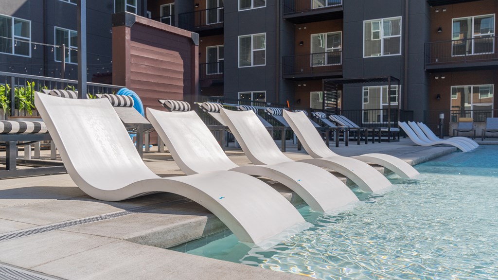 A row of white lounge chairs are arranged on the edge of a pool.