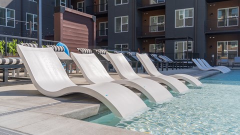 A row of white lounge chairs are arranged on the edge of a pool.