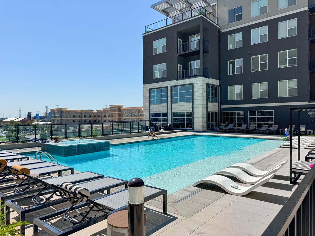 A large swimming pool with sun loungers and a building in the background.