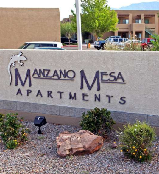 A large rock sits in front of a sign for Manzano Mesa Apartments.