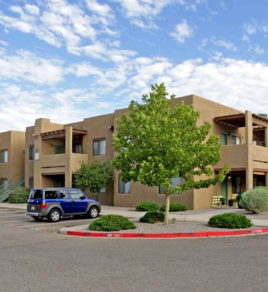 A blue car is parked in front of a tan building.