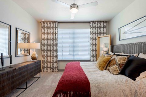 A bedroom with a bed, a red blanket, and a ceiling fan.