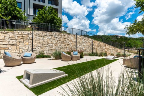 A modern outdoor seating area with a stone wall and wicker chairs.