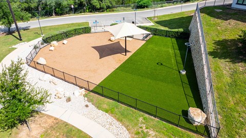 A dog park with a sand pit and a fence.