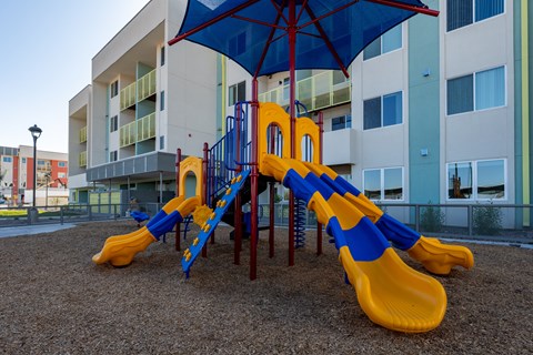 A playground with a blue umbrella and yellow slides.