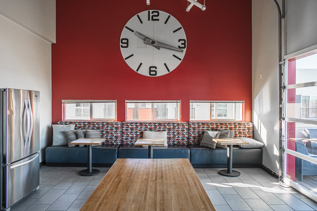 a large clock on a red wall in a lounge with booths and tables
