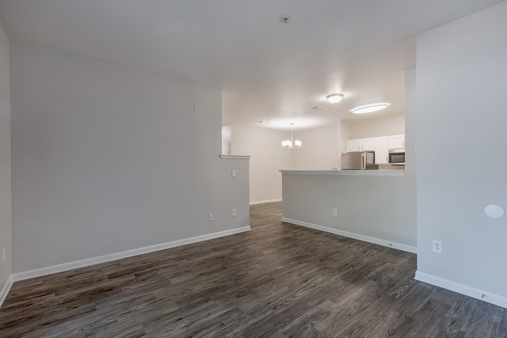 an empty living room and kitchen with wood flooring and white walls