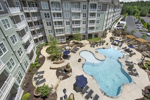 An aerial view of a pool and patio area in front of a large apartment building.
