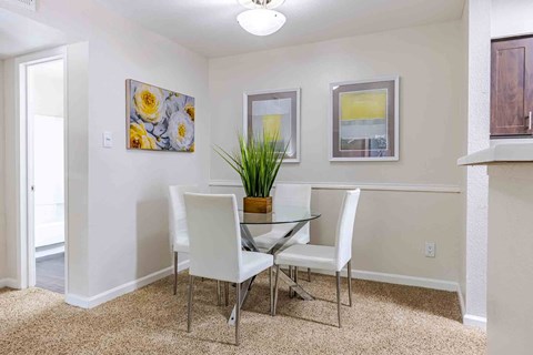 A dining room with a glass table and white chairs.