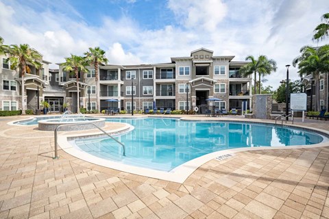 A large swimming pool is surrounded by a brick patio and palm trees.