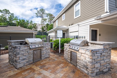 Two stone BBQs are in a courtyard in front of a house.