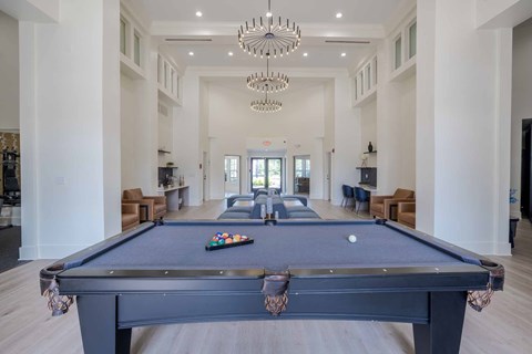 A pool table is in the middle of a large room with a chandelier hanging from the ceiling.