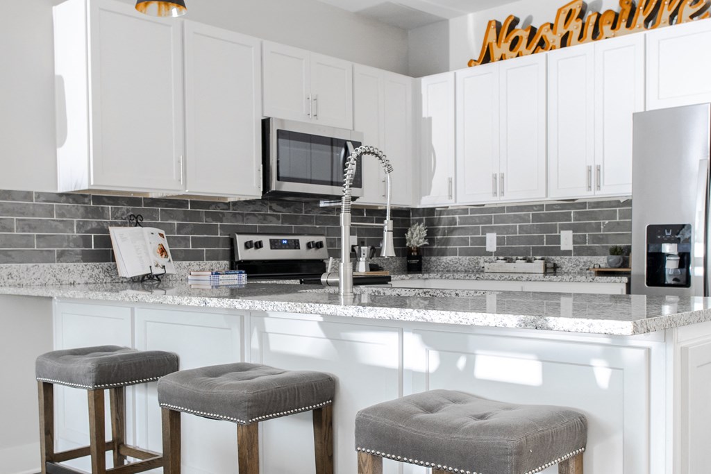 a kitchen with white cabinets and a counter with three stools