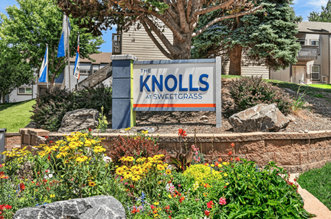 A sign that says "The Knolls at Sweetgrass" is in front of a flower bed.