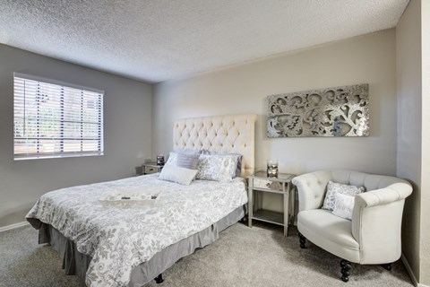 A bedroom with a bed, chair, and window.
