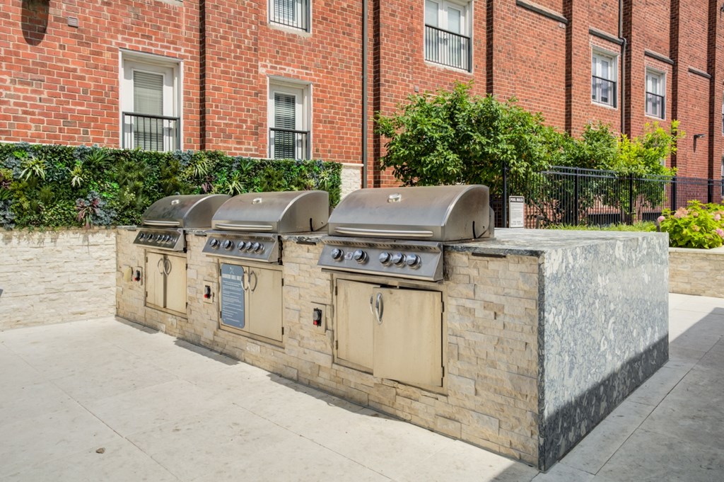 Three outdoor grills are lined up on a stone wall.
