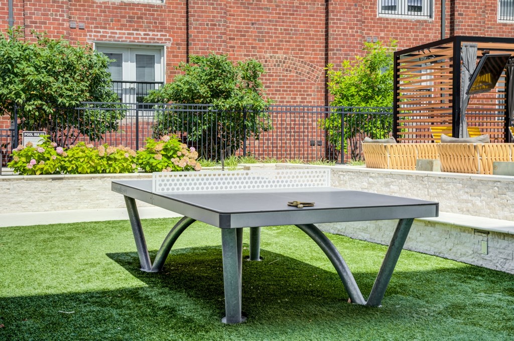 A rectangular table with a metal frame and a wooden top is placed on a green lawn.