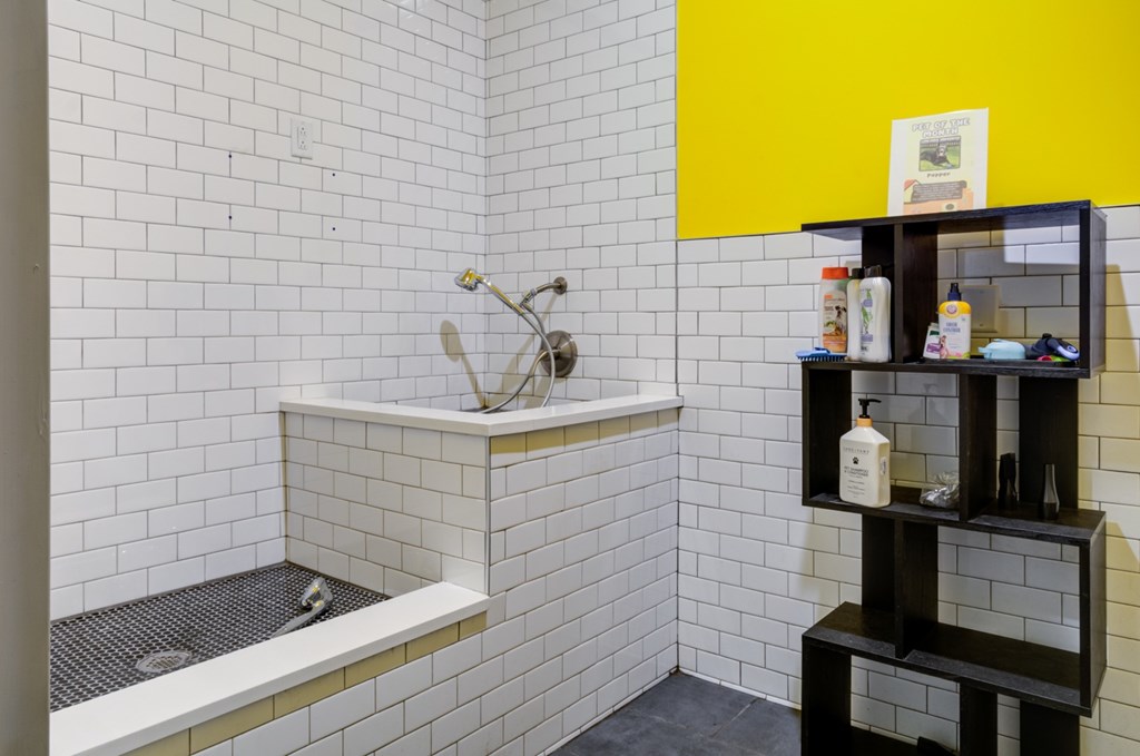 A bathroom with a white tiled shower and a black shelf with various toiletries.