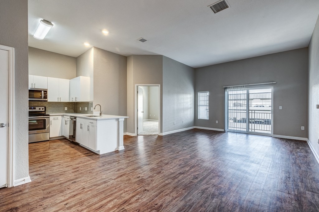 an empty living room with a kitchen and a large window