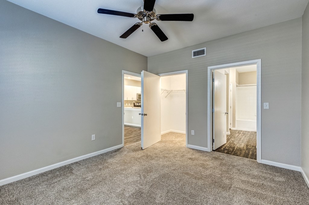 an empty living room with a ceiling fan and a door to a bathroom
