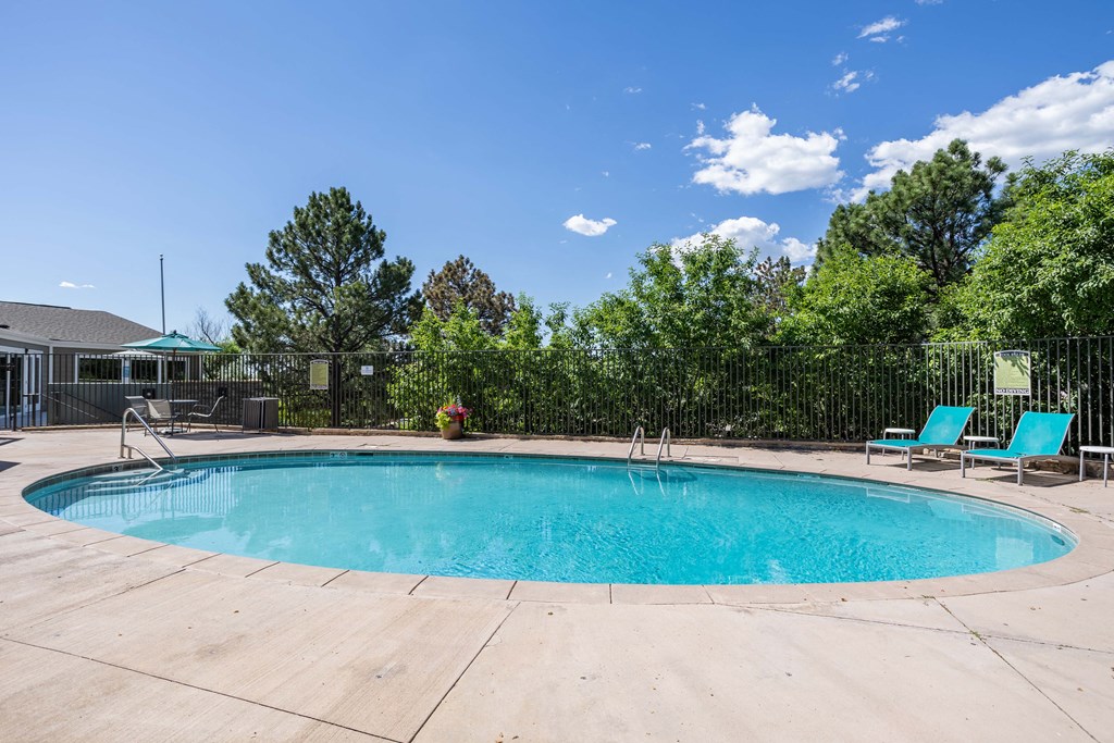 a swimming pool with blue chairs and trees and a house in the background