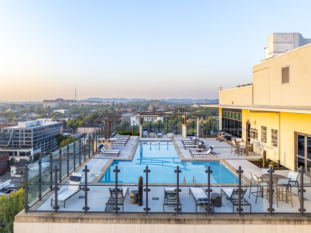 A rooftop pool with a glass railing and lounge chairs.