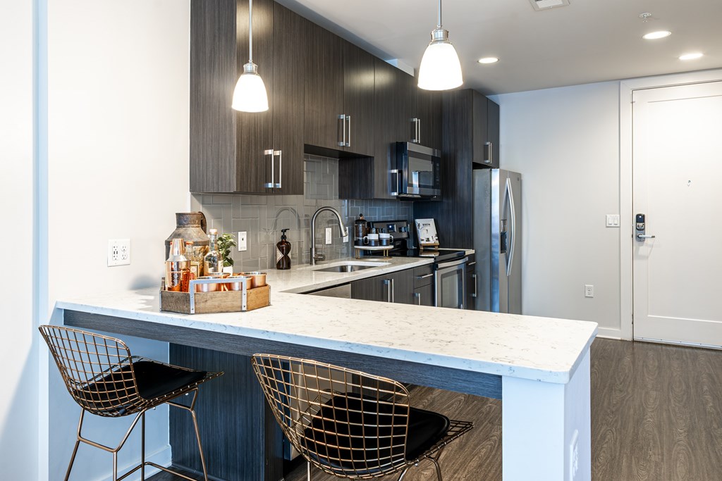 A modern kitchen with a white island and black chairs.
