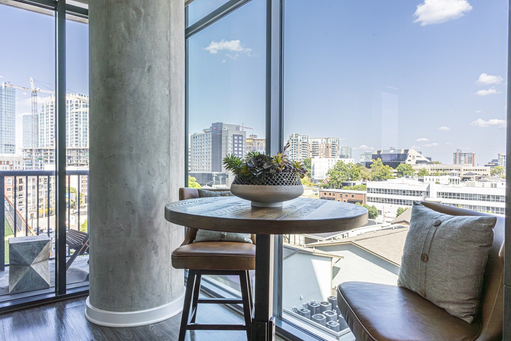 A round table with a plant on it and a pillow on a chair in front of a window with a view of a city.