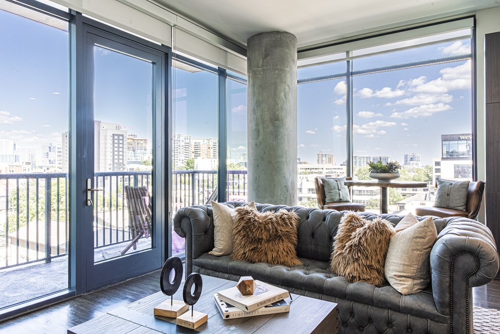 A black couch with pillows sits in a room with a view of the city.