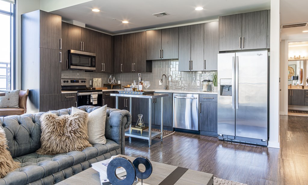 A modern kitchen with a grey couch and a wooden floor.